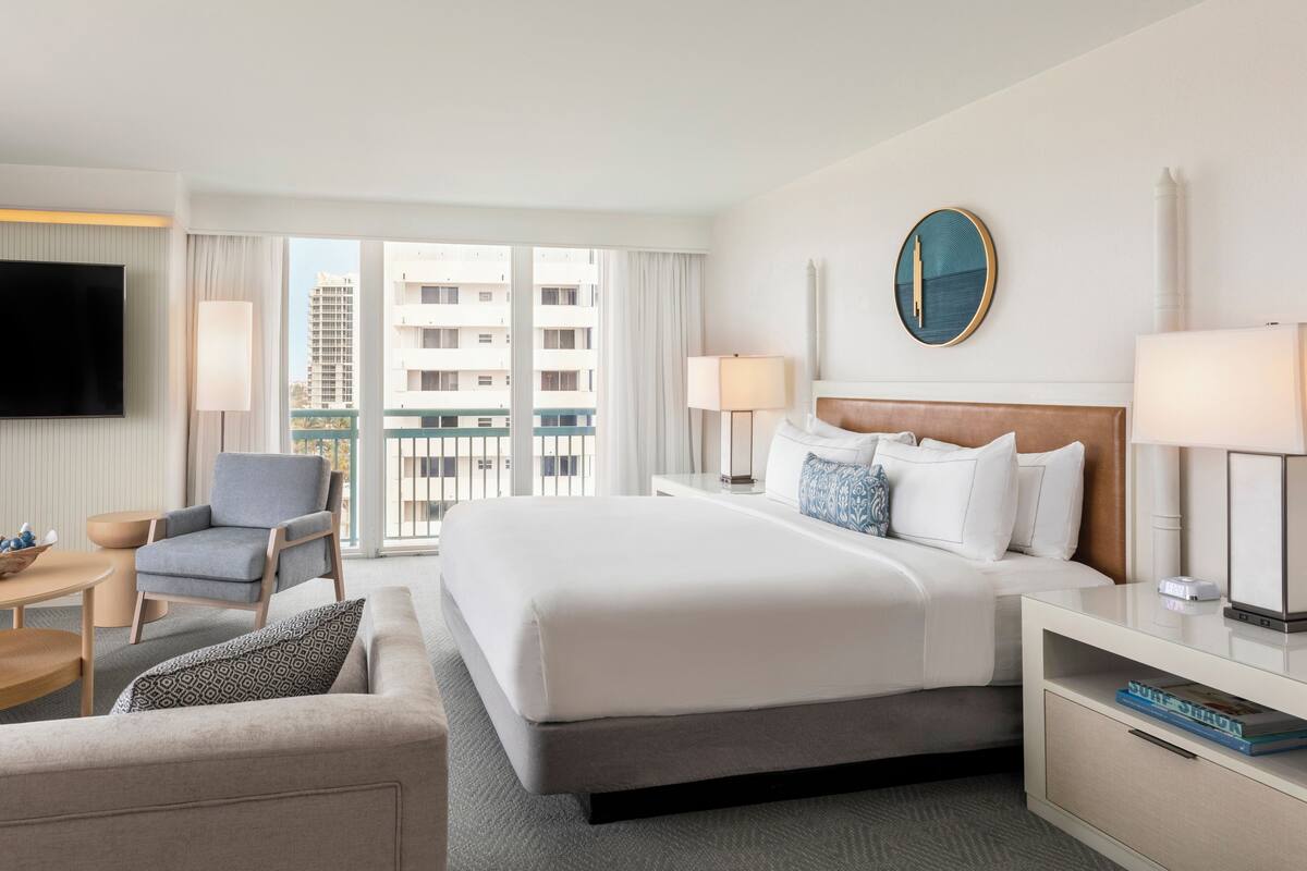 A hotel room with a large bed, a desk, a chair, and a TV.