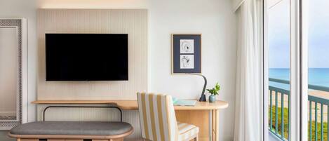 Une chambre d’hôtel comprenant un lit, un bureau avec une chaise, une télévision et une grande fenêtre donnant sur la plage.