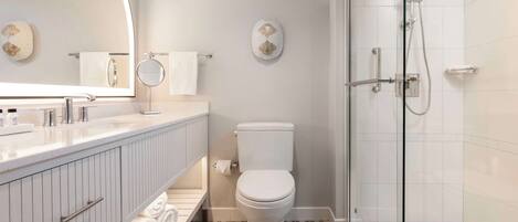 Un baño moderno con cabina de ducha de vidrio, inodoro blanco y tocador con espejo.