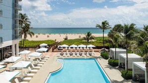 A resort pool area with lounge chairs and umbrellas, a beach view, and a clear sky. - The Singer Oceanfront Resort, Curio Collection by Hilton (Singer Island)