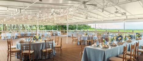 Un espace extérieur aménagé pour les événements, avec des tables dressées pour les repas, entouré d’une structure métallique blanche et surmonté d’un auvent.