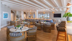 A spacious indoor dining area with wicker furniture, a central bar, and a large TV screen. - The Singer Oceanfront Resort, Curio Collection by Hilton (Singer Island)