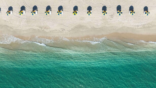 A beach with rows of beach umbrellas and a sandy shoreline. - The Singer Oceanfront Resort, Curio Collection by Hilton (Singer Island)