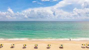 A beach with clear turquoise water, a sandy shore, and several beach umbrellas.