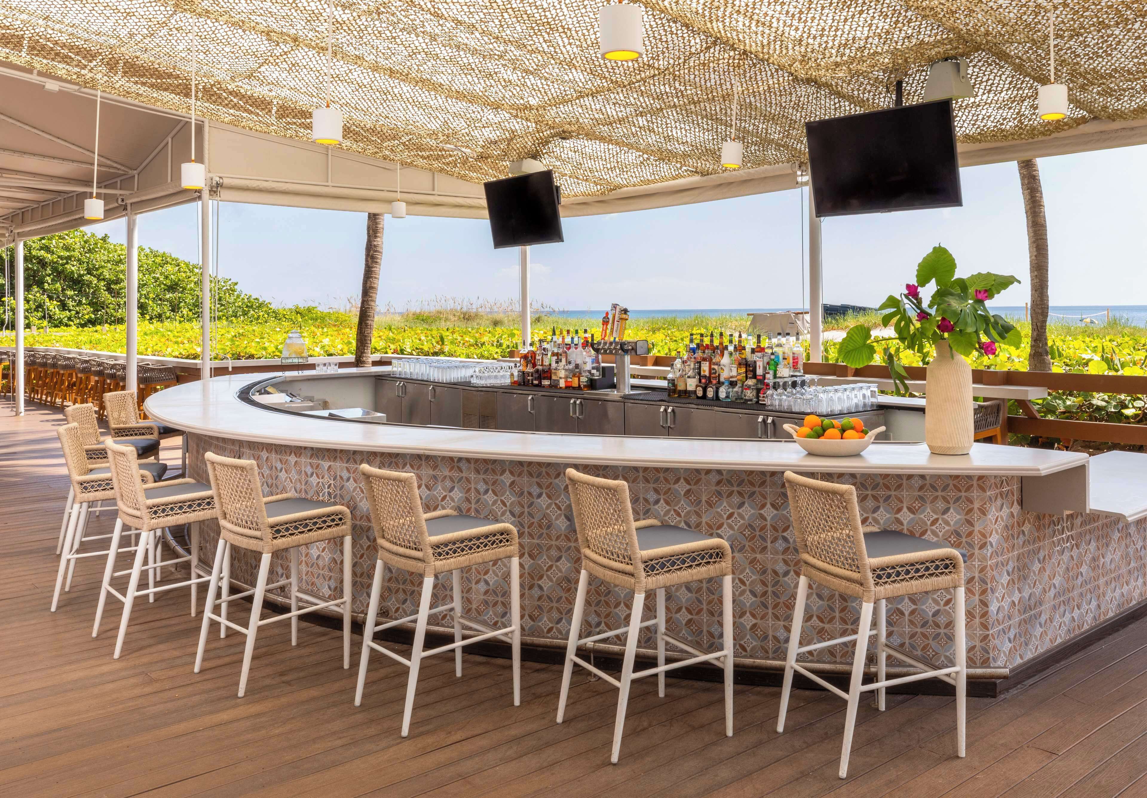 A bar area with a curved counter, wicker bar stools, and a view of the ocean.