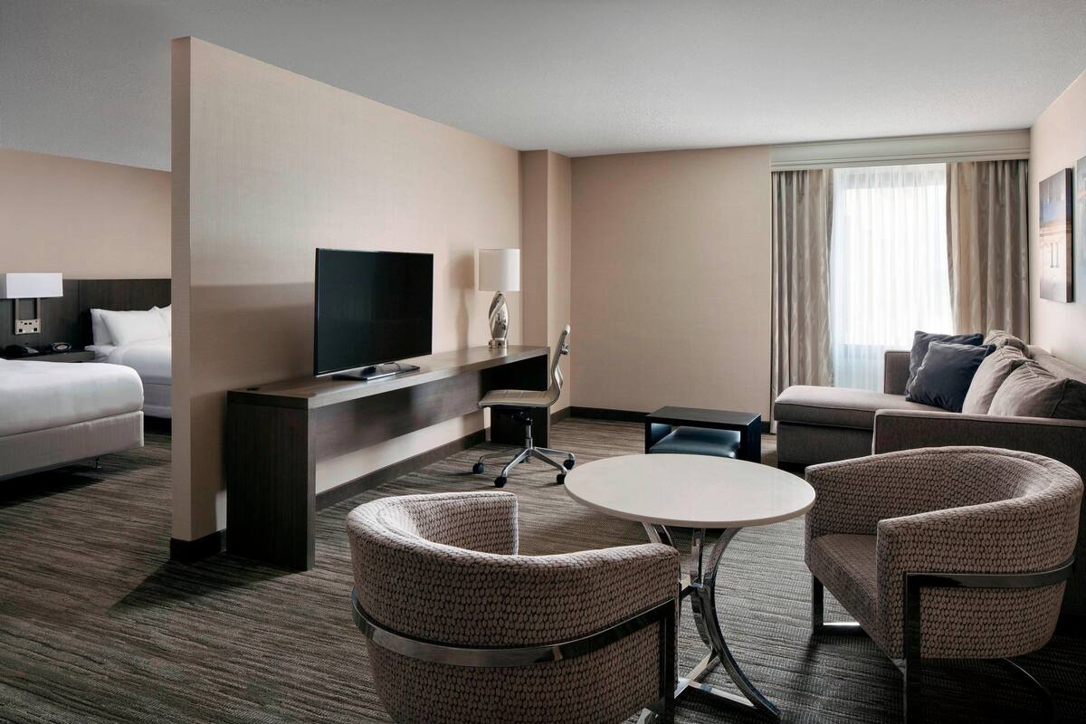 A hotel room with a bed, a TV, a desk, a chair, a sofa, and a dining table.