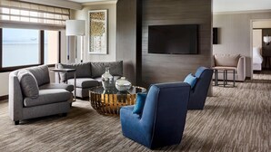 Una habitación de hotel moderna con un ventanal grande, un televisor de pantalla plana, un sofá, un sillón azul y una mesa de centro.