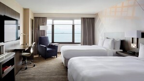 Habitación de hotel con dos camas, un escritorio con silla, televisión y vista al mar.