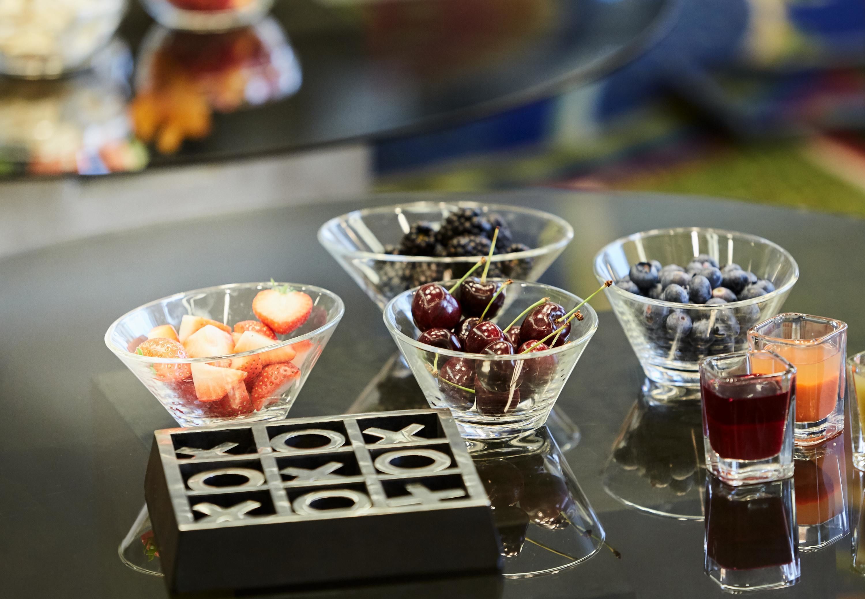 Ein Buffet mit durchsichtigen Glasbehältern, gefüllt mit Erdbeeren, Kirschen und Blaubeeren, sowie kleinen Gläsern mit roten und orangen Getränken.