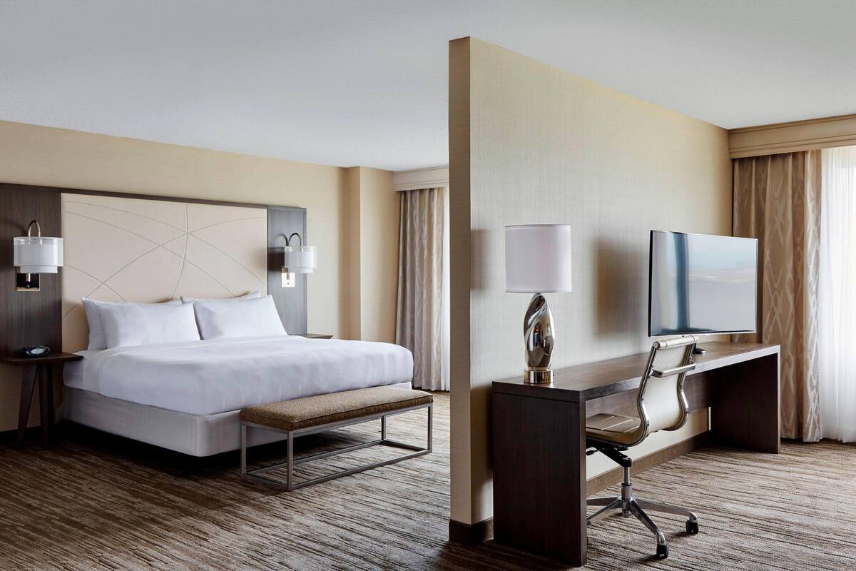 A hotel room with a bed, desk, chair, and television.