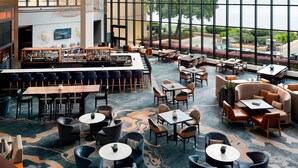 A spacious indoor area with a bar, multiple seating arrangements, and large windows offering a view of the outdoors.