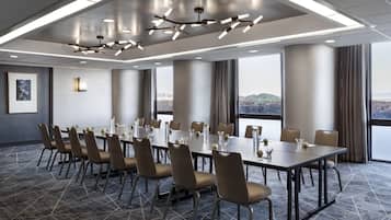 A conference room with a long table, chairs, and a city view through large windows.