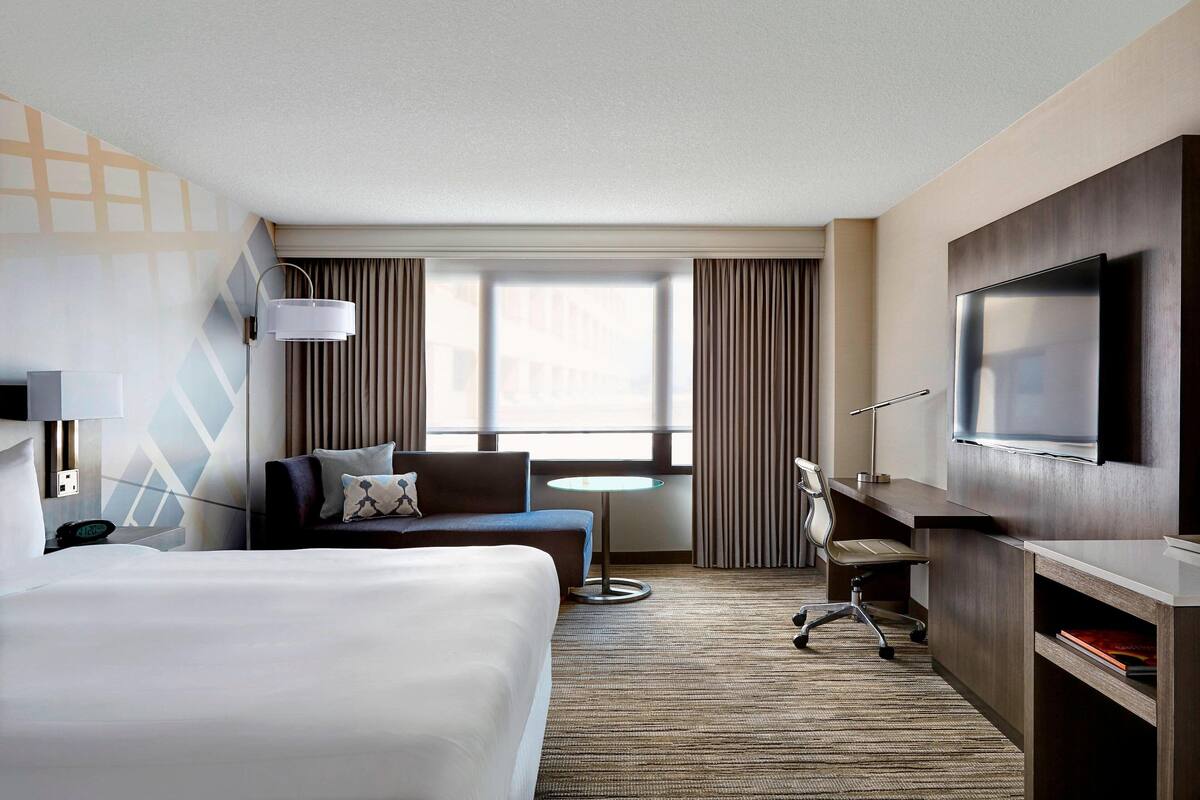 A hotel room with a large bed, a desk, a TV, a sofa, and a window with curtains.