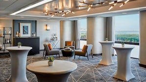 Un vestíbulo de hotel moderno con mesas redondas, asientos cómodos, una zona de bar y ventanas amplias que ofrecen vistas de la ciudad.