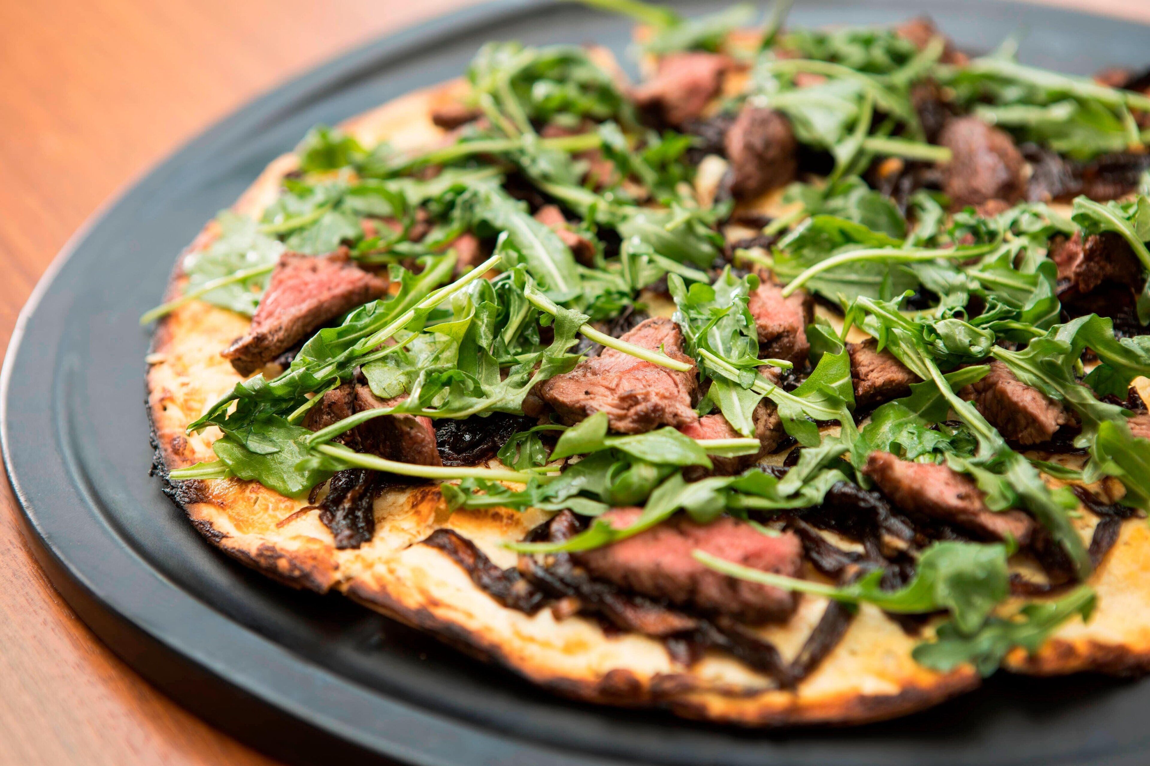 A pizza with meat and greens on a plate.