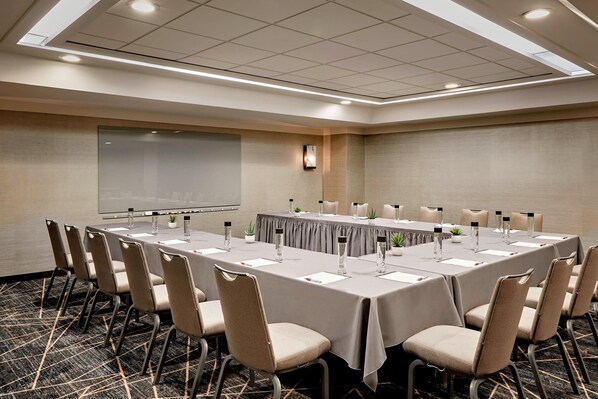 A conference room with a long table, chairs, a projector screen, and a carpeted floor.