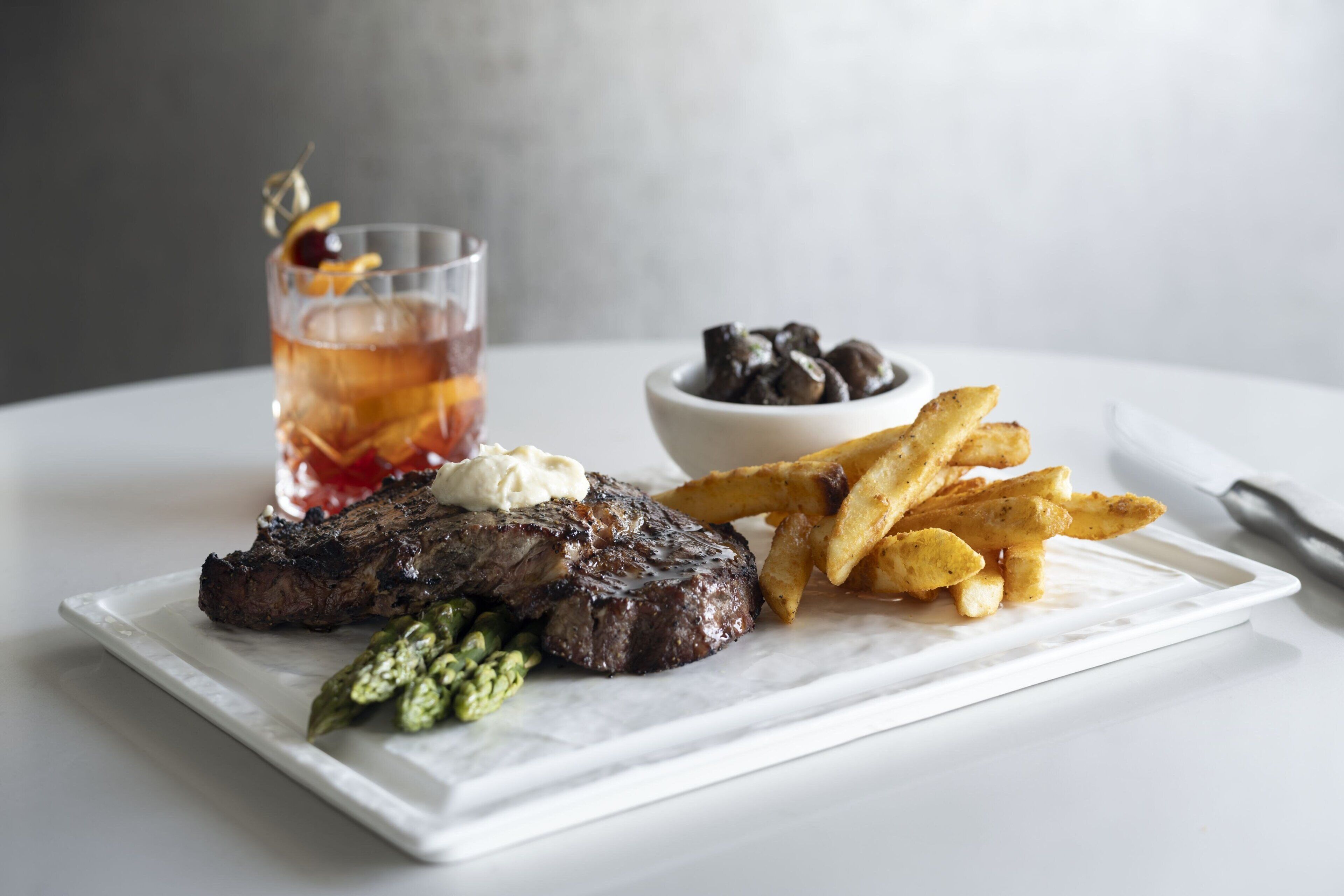 A steak with fries and a drink on a white plate.