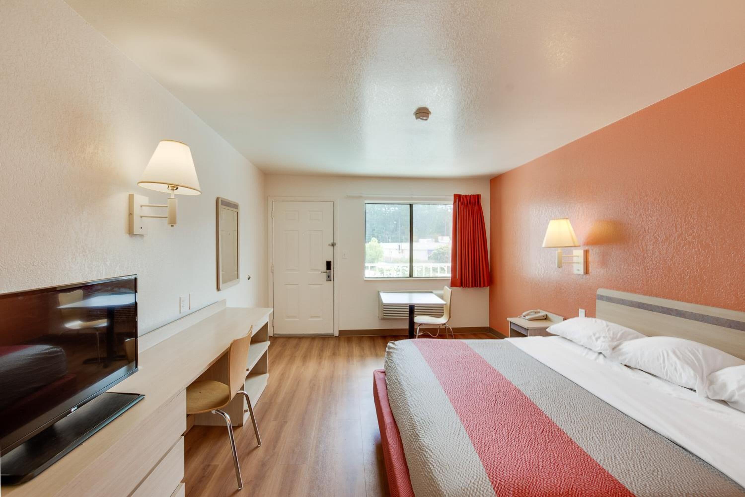 A hotel room with a bed, desk, chair, TV, and two wall lamps.