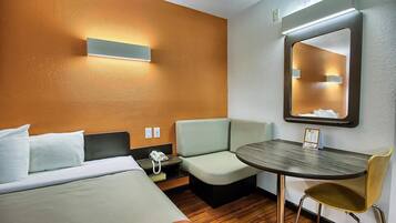 A hotel room with a bed, a desk with a chair, a small table, and a mirror.