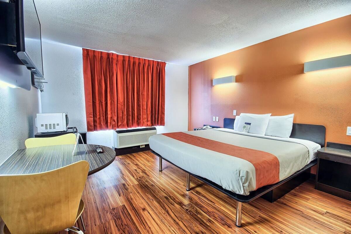Une chambre d’hôtel avec un lit, des tables de chevet, un bureau, une chaise, un rideau rouge et un projecteur.