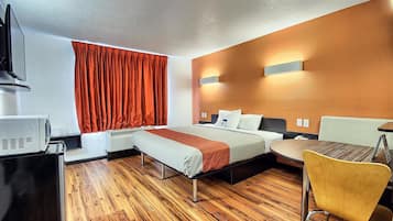 A hotel room with a bed, a desk with a coffee machine, a chair, and a wall-mounted TV.