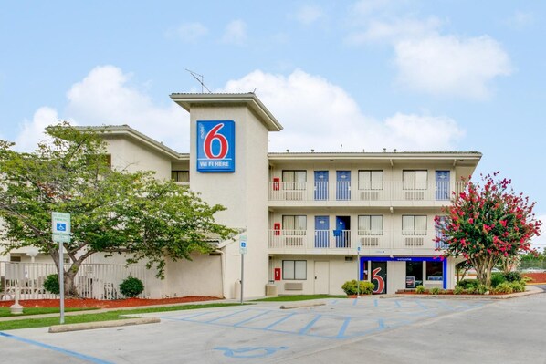 Un motel con un letrero que dice '6', un estacionamiento y un edificio con varios balcones.