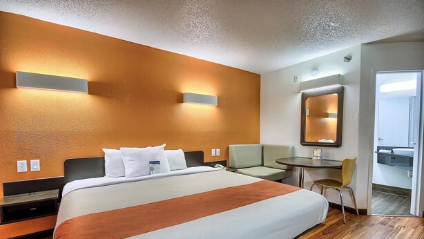 Une chambre d’hôtel avec un grand lit, une petite table, une chaise et une salle de bain visible à travers une porte ouverte.