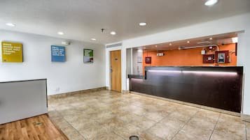 A hotel lobby with a reception desk, tiled flooring, and several informational posters on the walls.