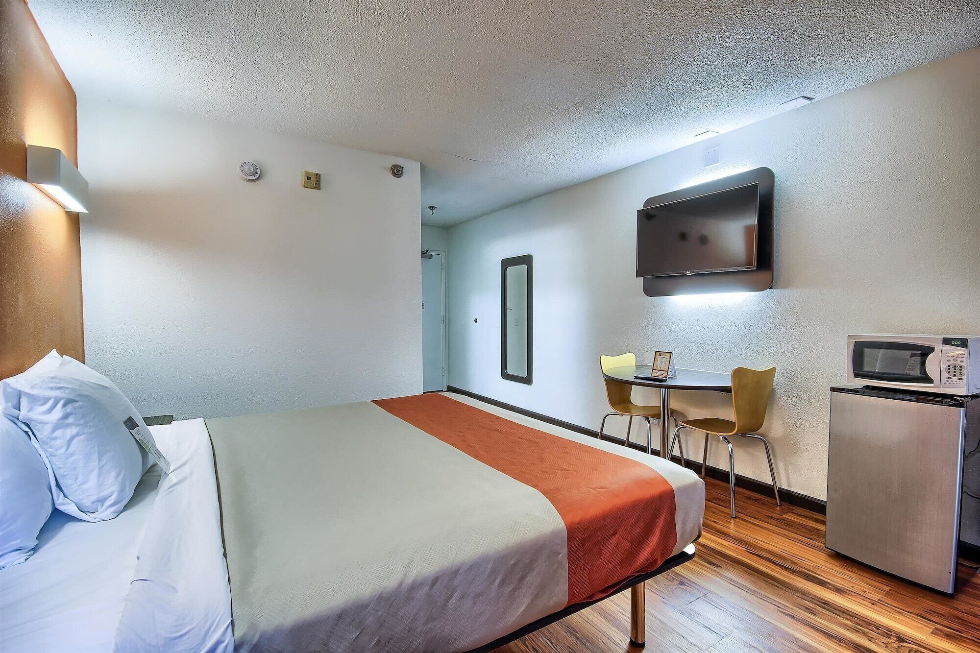 A hotel room with a bed, a desk with a chair, a television, and a microwave.