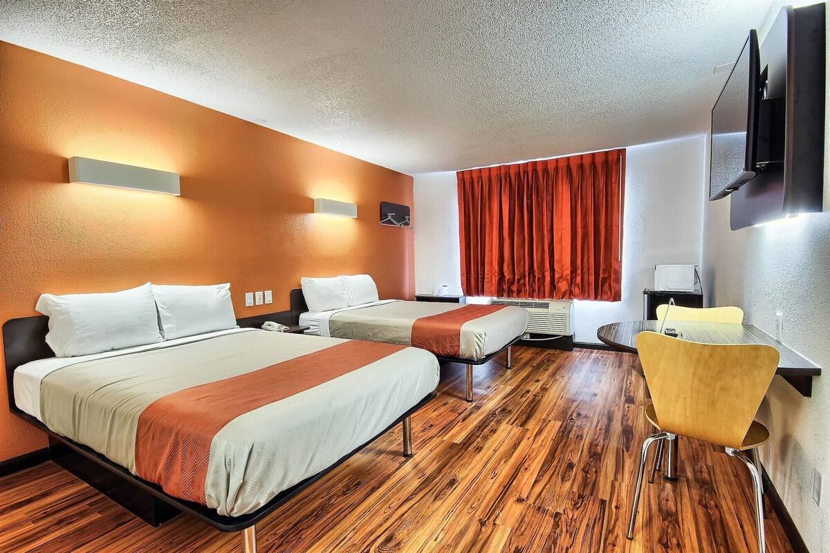 Une chambre d’hôtel avec deux lits, un plancher en bois, un rideau rouge, une télévision et une chaise jaune.