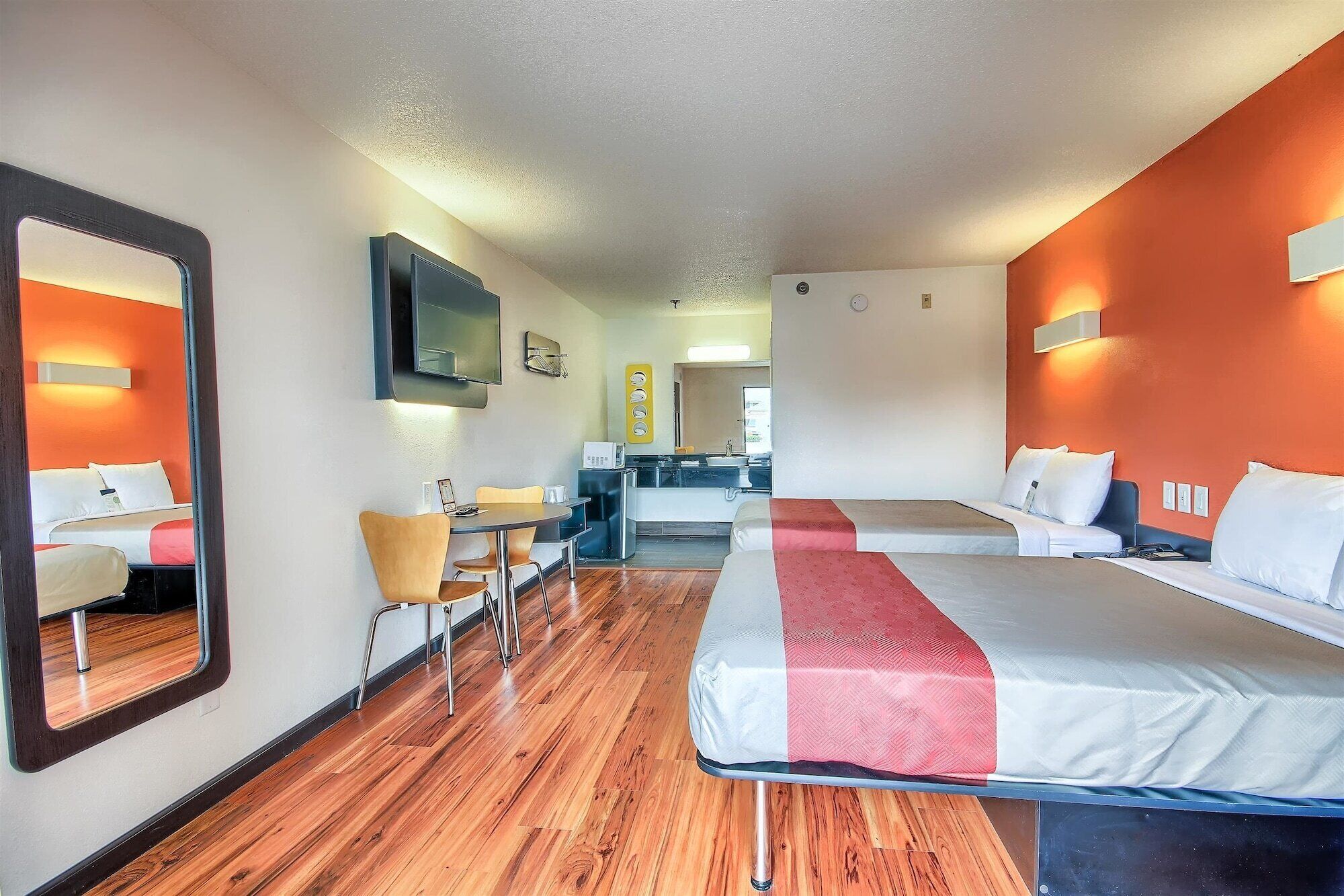 A hotel room with two beds, a desk, a chair, a TV, and a mirror.