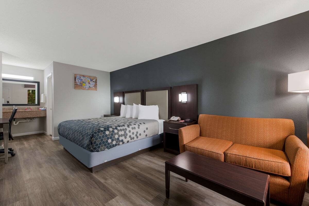 Ein Hotelzimmer mit Bett, Schreibtisch, Sessel, Sofa und Nachttisch.