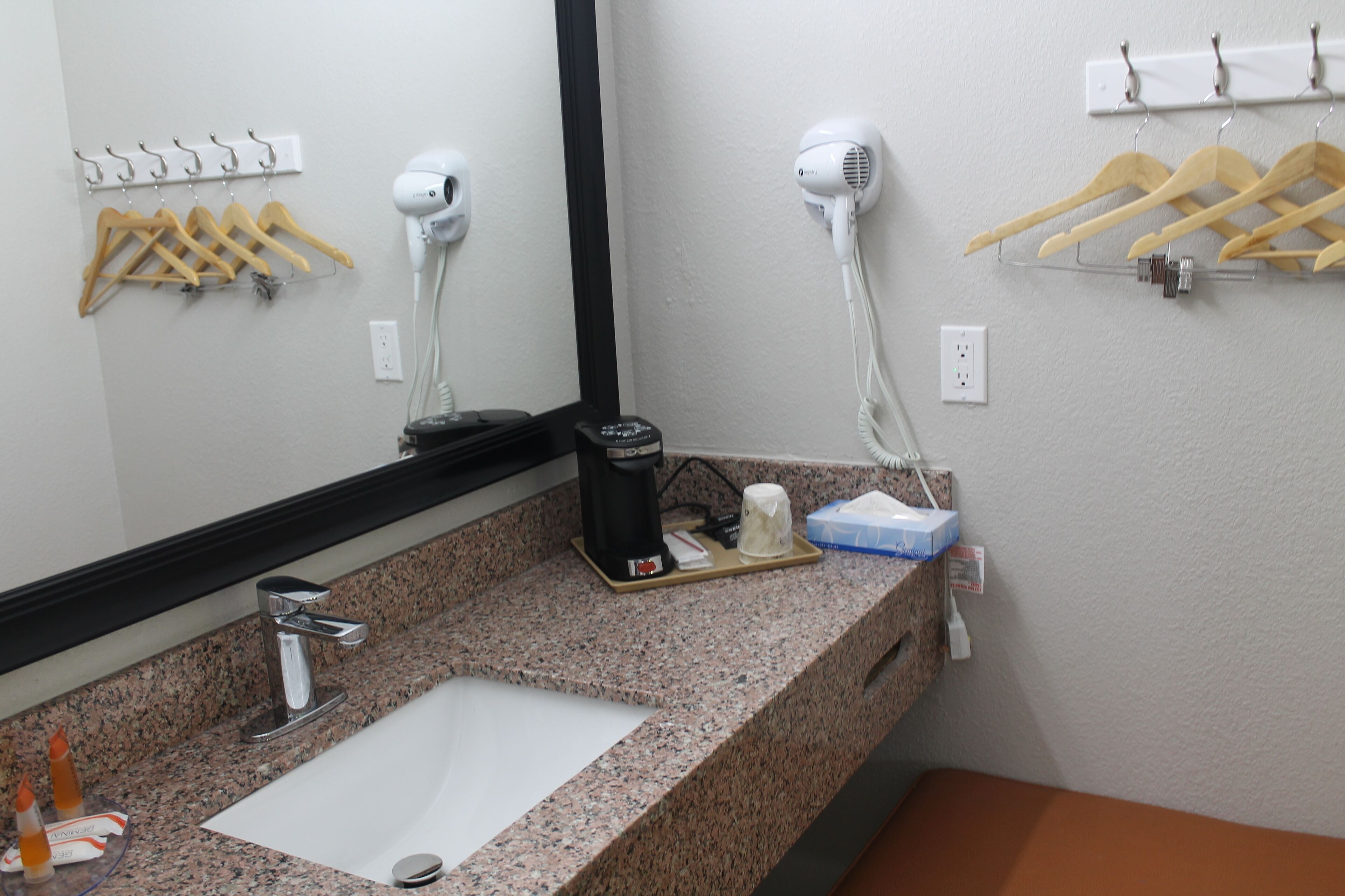 A bathroom with a granite countertop, a sink, a mirror, a hairdryer, and wooden hangers on a rack.