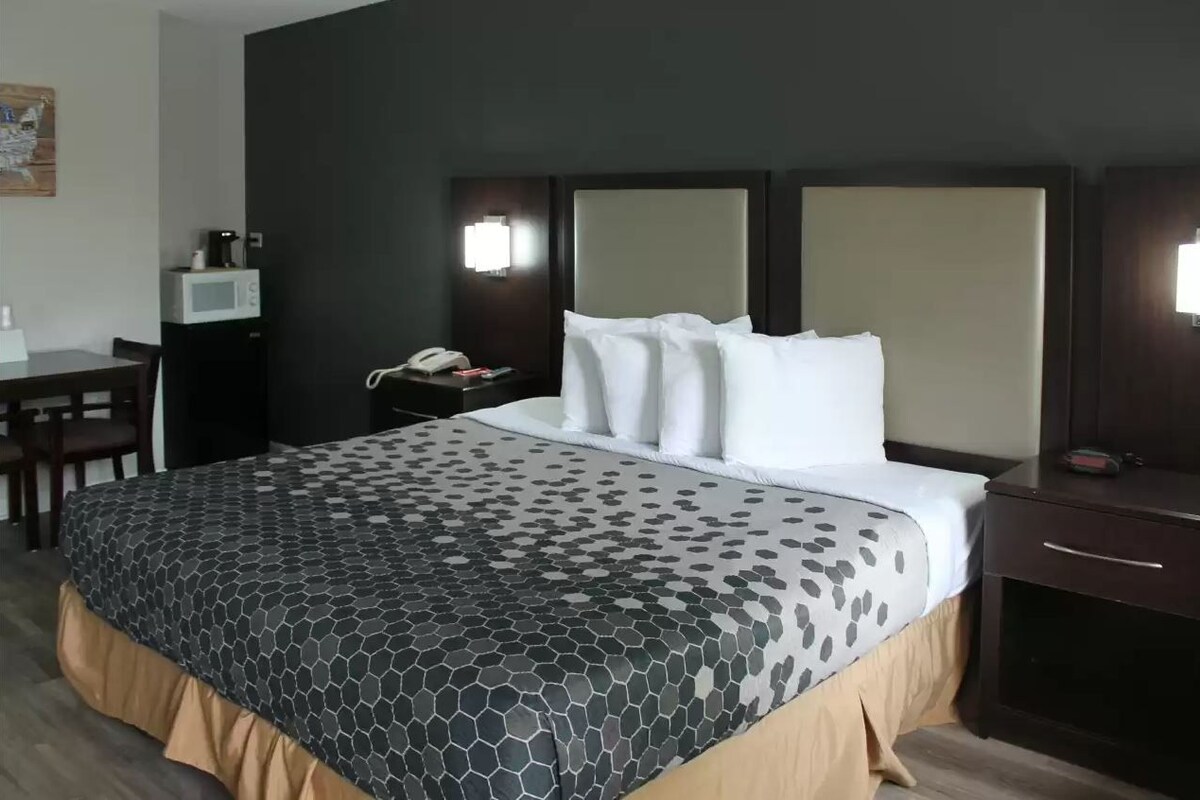 A hotel room with a large bed, a desk with a telephone, a microwave, and a nightstand with a lamp.
