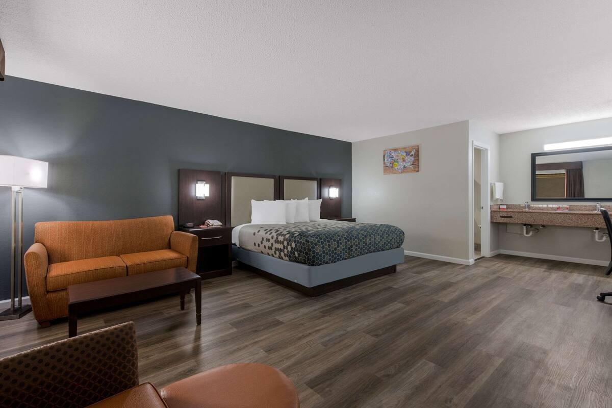 Ein Hotelzimmer mit Bett, Sofa, Schreibtisch, Stuhl, Nachttisch, Lampe, Spiegel und einem Badezimmer mit Waschbecken und Spiegel.