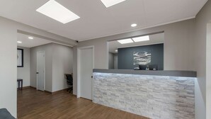 Un área de recepción con mostrador de textura de piedra, luces empotradas en el techo y una puerta que da a otra habitación.