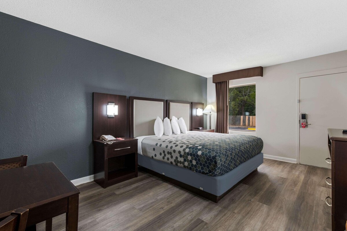 A hotel room with a bed, bedside tables, a desk, and a window with curtains.