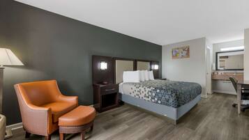 A hotel room with a bed, a chair, a desk, and a lamp.