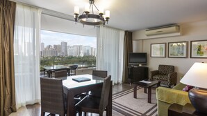 A hotel room with a dining area, a sofa, a TV, and a balcony with a city view. - Regency on Beachwalk Waikiki by OUTRIGGER (Honolulu)