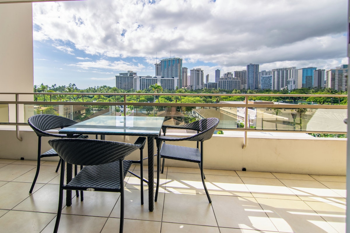 A balcony with a glass table and chairs, a city skyline view, and a tiled floor.