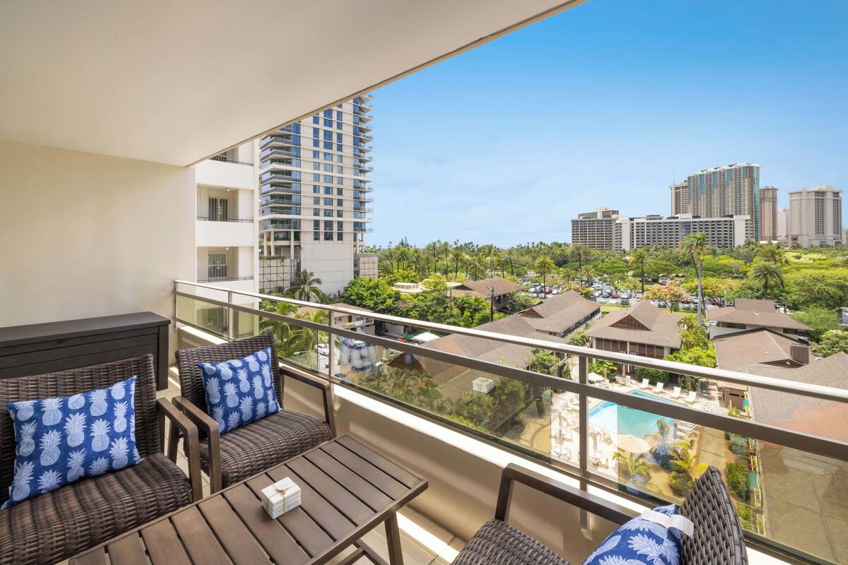 A balcony with wicker furniture and a view of a cityscape and a swimming pool.