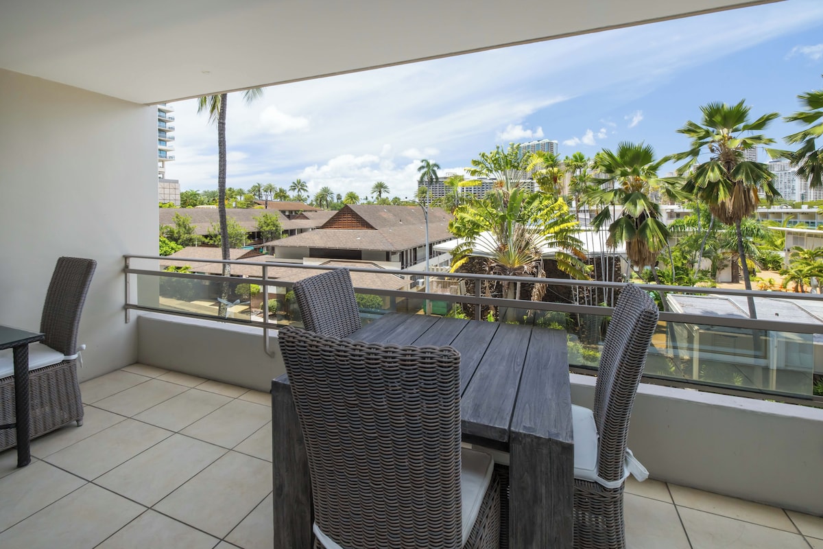 A balcony with wicker furniture, a view of palm trees and buildings.