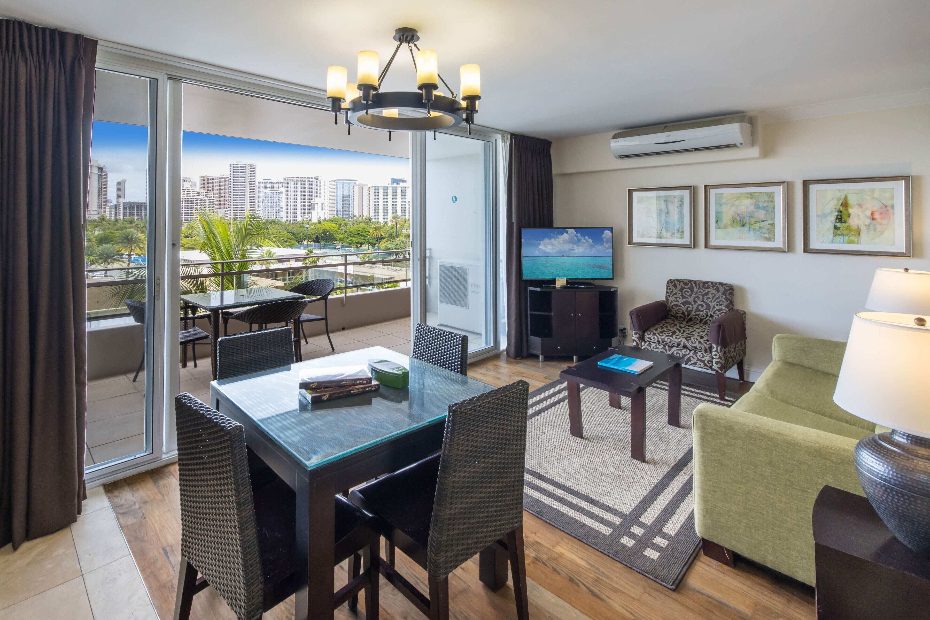 A modern hotel room with a balcony, a dining area, a TV, and artwork on the walls.