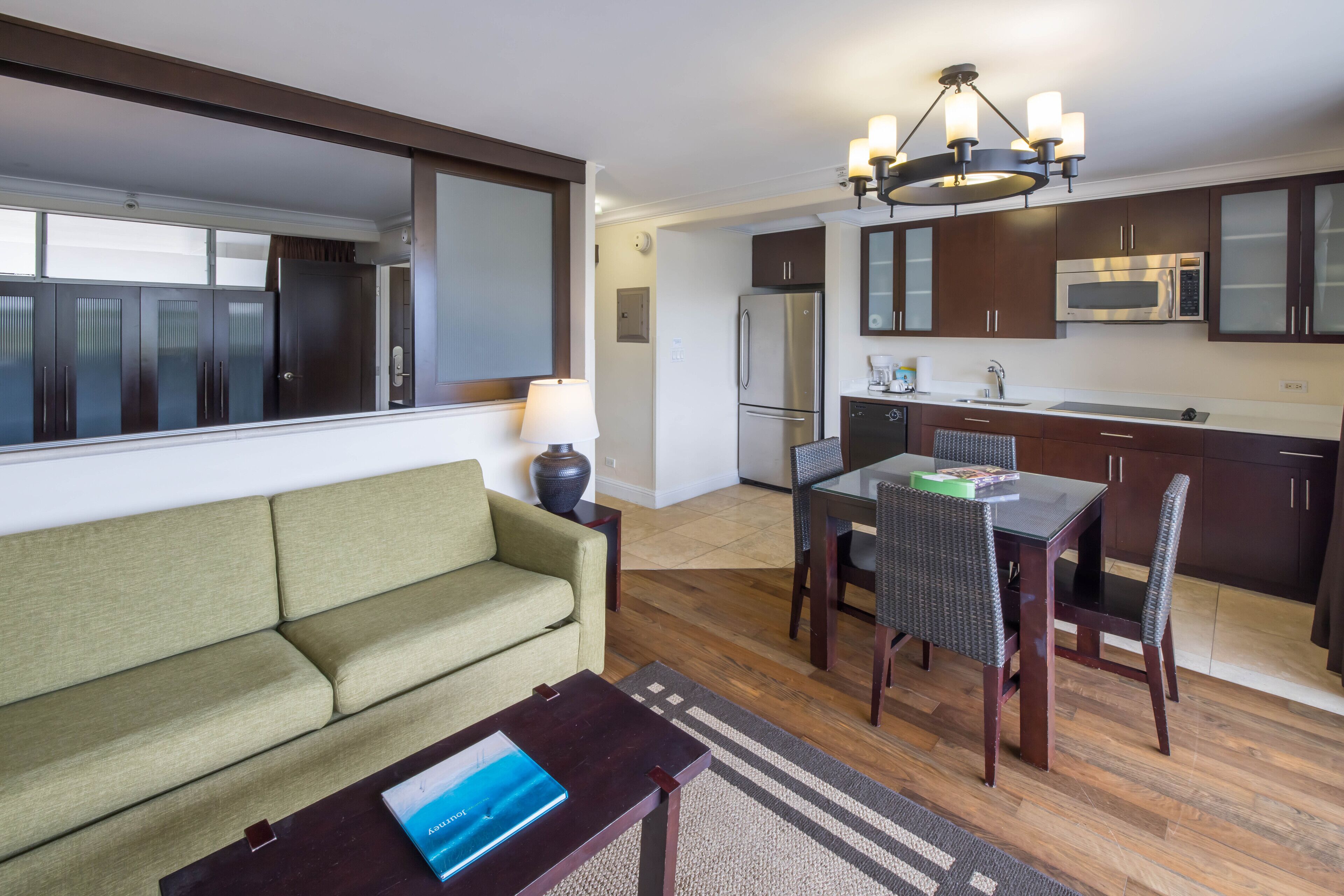 Una sala de estar moderna con un sofá, una mesa de comedor con sillas, y una cocina con refrigerador, microondas y alacenas.