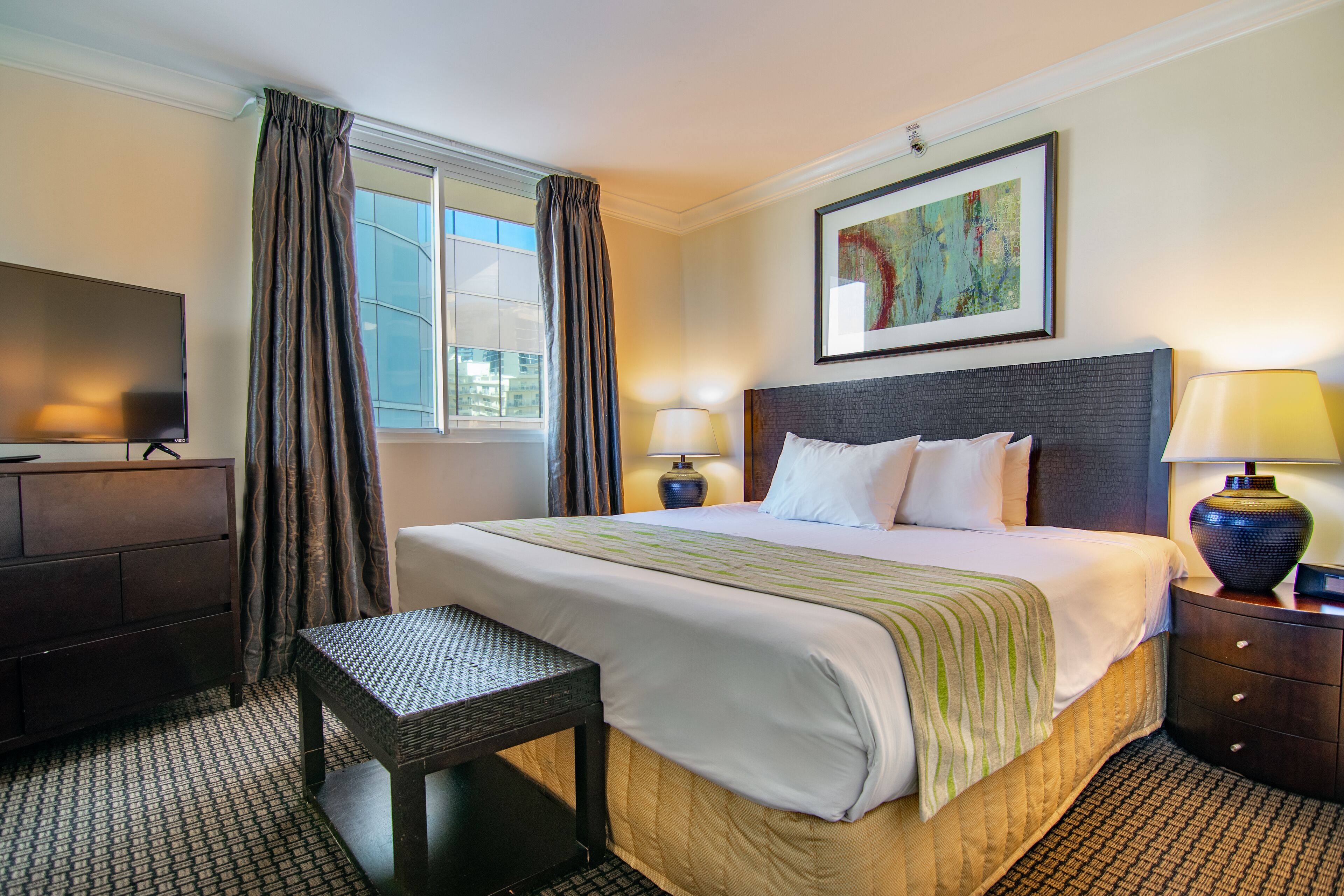 A hotel room with a large bed, a desk, a chair, a TV, and a window with curtains.