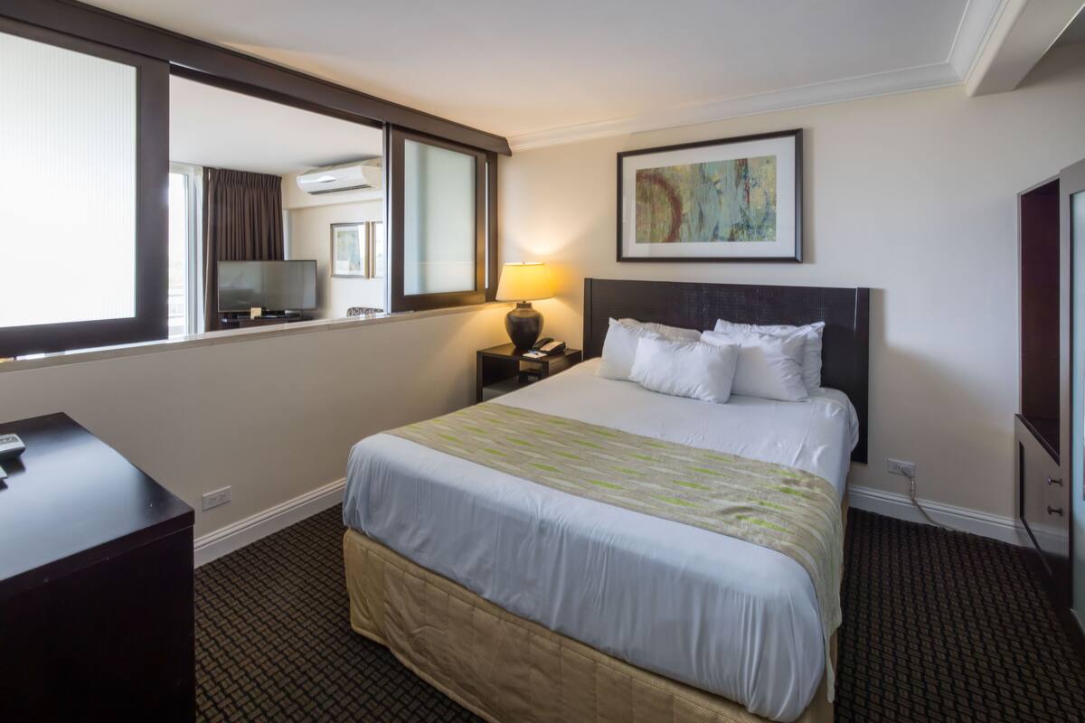 A hotel room with a large bed, a desk, a TV, and a painting on the wall.