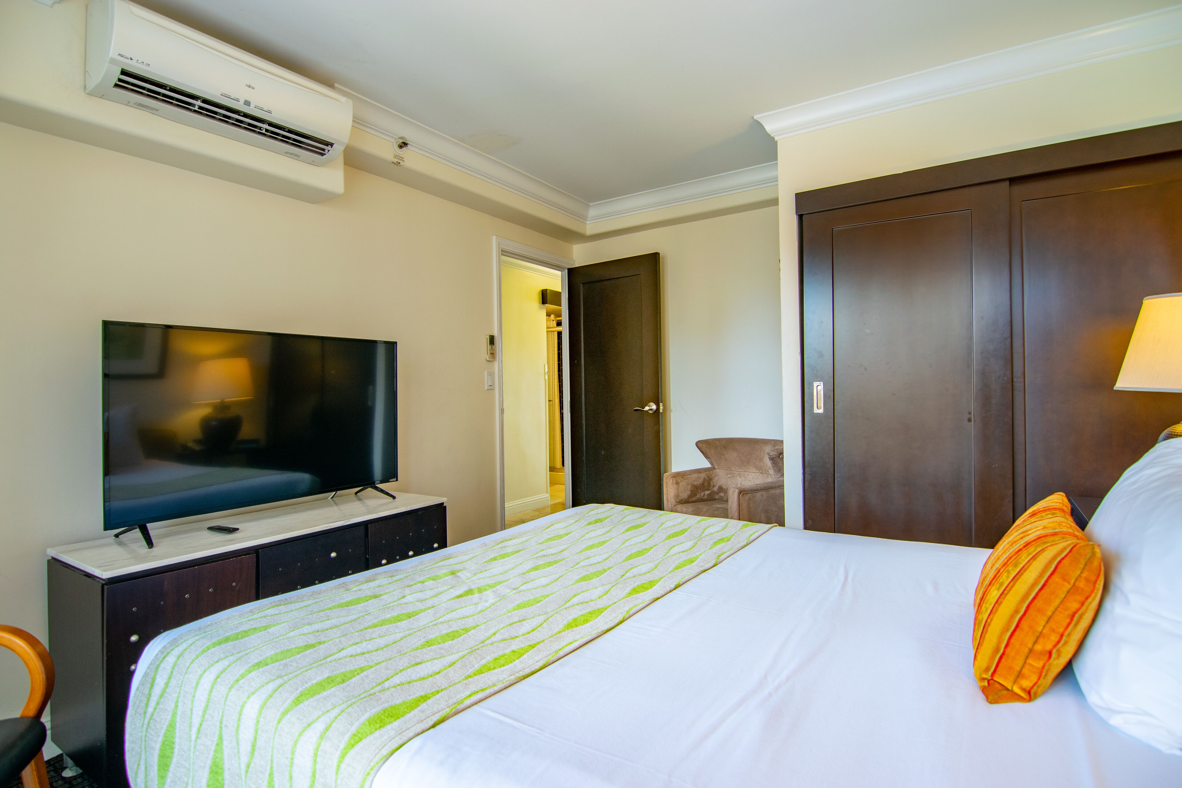 A hotel room with a bed, a television, a wardrobe, and an air conditioning unit.