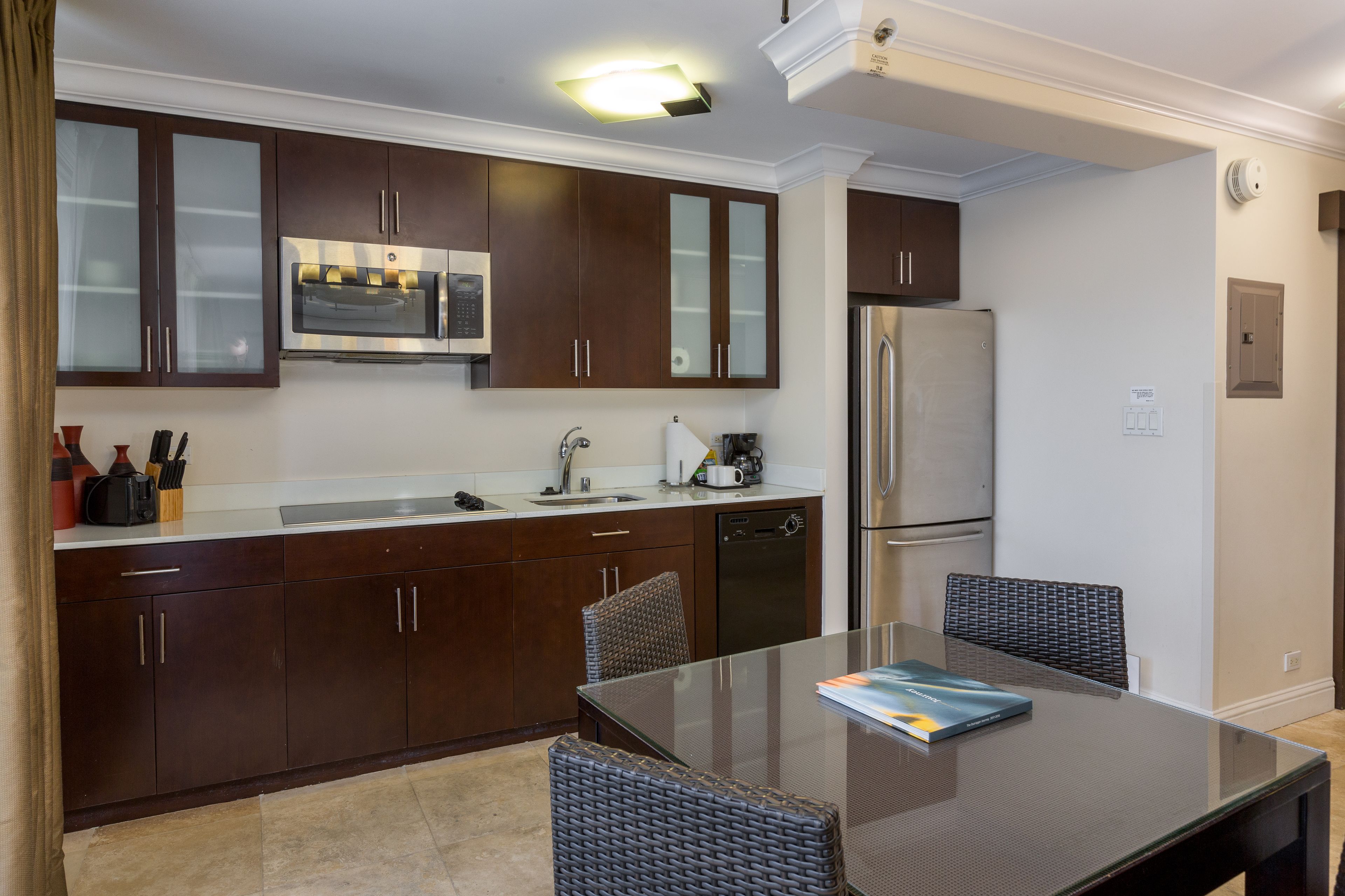A modern kitchen with dark wooden cabinets, stainless steel appliances, and a glass dining table.