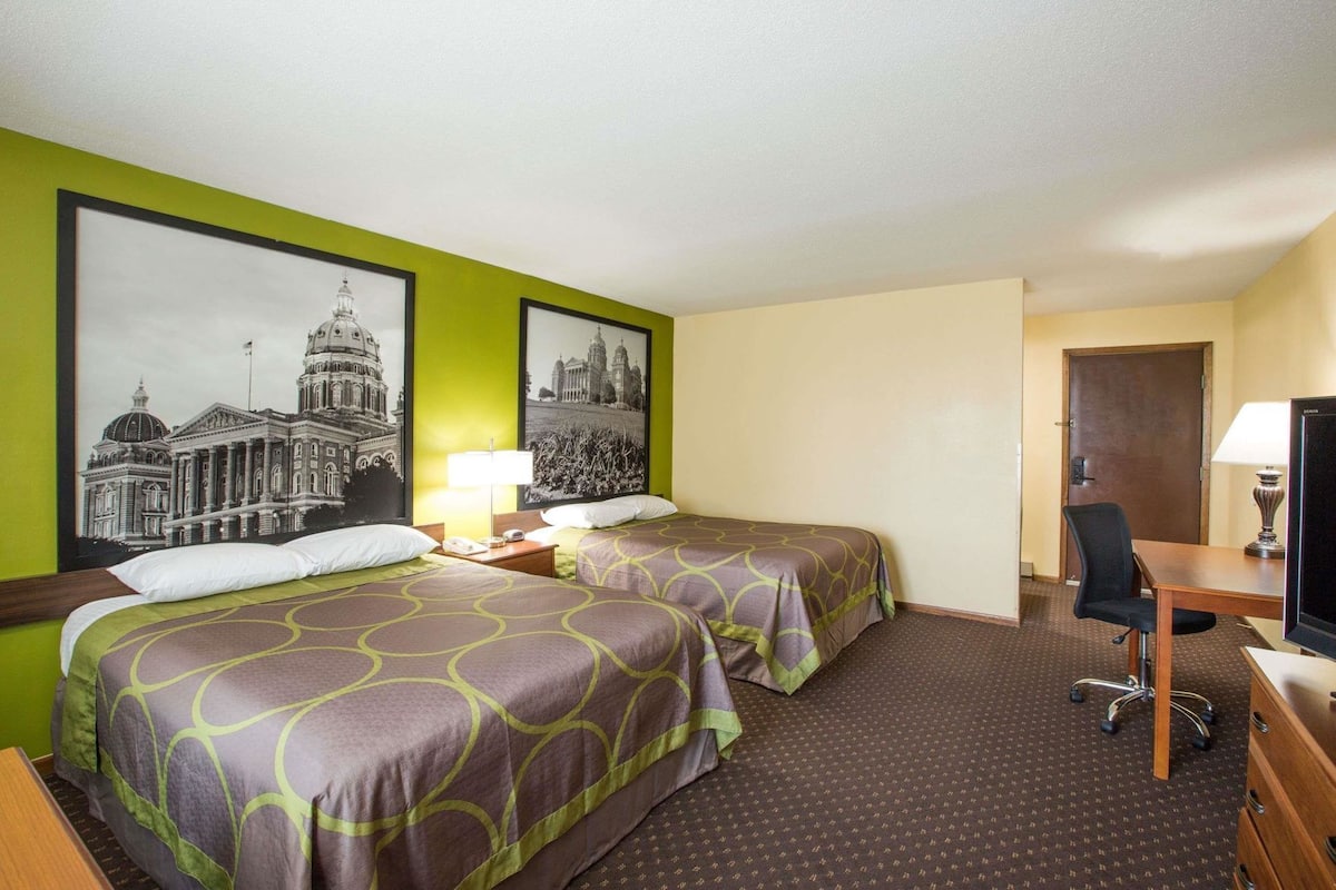 A hotel room with two beds, a desk, a chair, a TV, and two framed pictures on the wall.