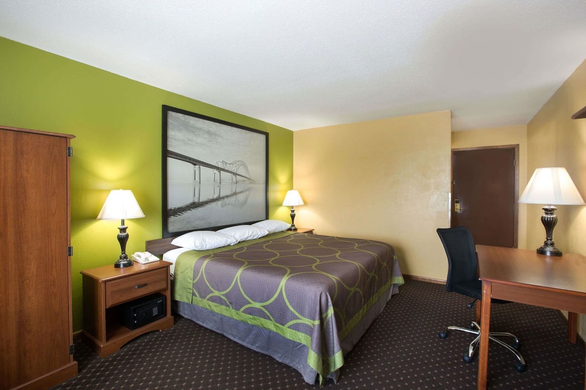 A hotel room with a bed, two bedside tables with lamps, a desk with a chair, and a door.